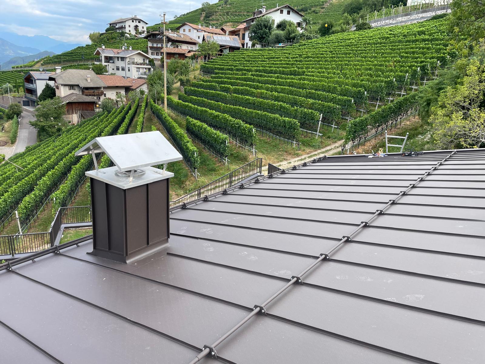 Tetto in metallo scuro con aggraffature e rivestimento del camino, davanti ai vigneti